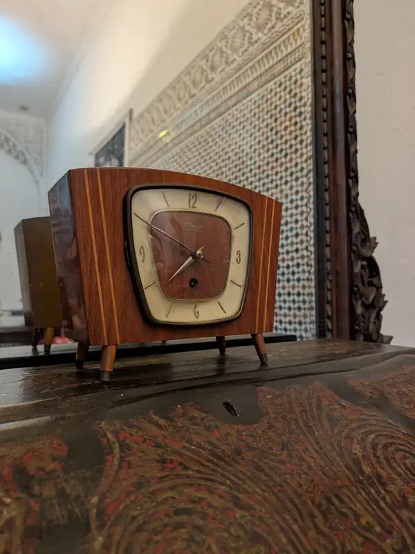 Pendule en bois à cadran carré, posée sur un meuble en bois peint