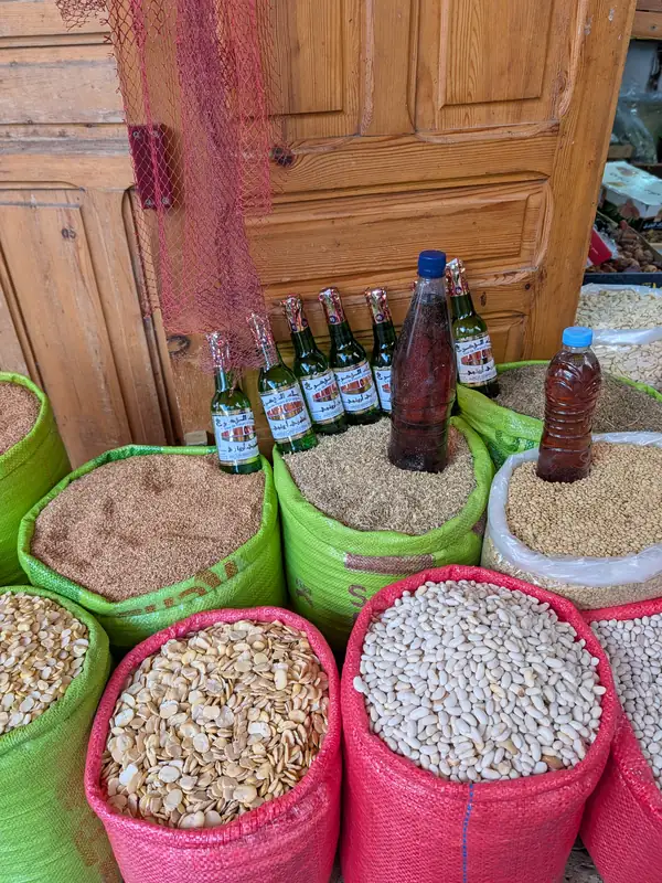 Sacs de légumes secs et de graines devant une boutique, bouteilles alignées au-dessus